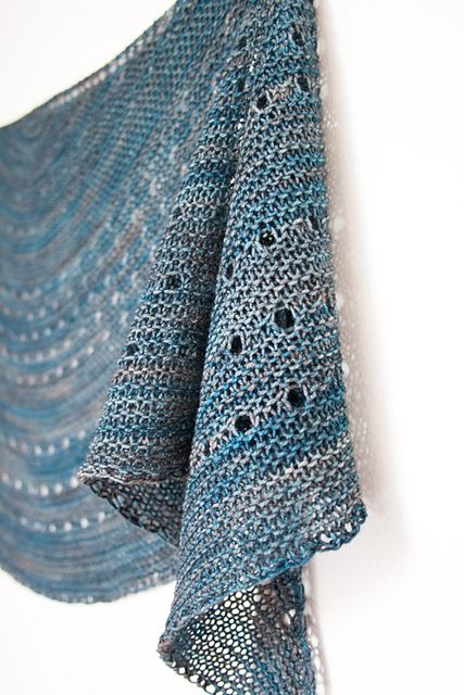 a blue crocheted shawl hanging from a hook on a white wall next to a cell phone