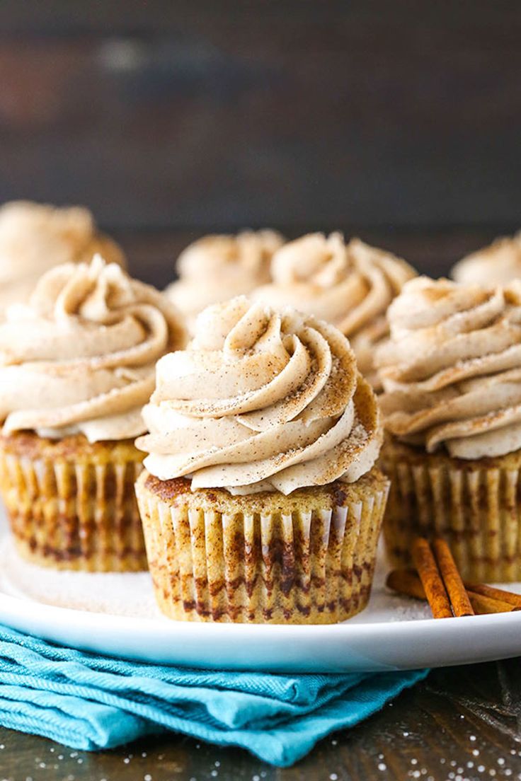 three cupcakes with frosting on a white plate next to some cinnamon sticks