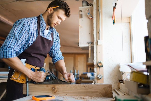 a man in an apron working on a piece of wood with a power driller