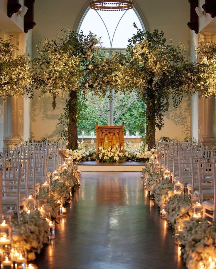 an indoor wedding venue with candles and flowers on the aisle, surrounded by greenery