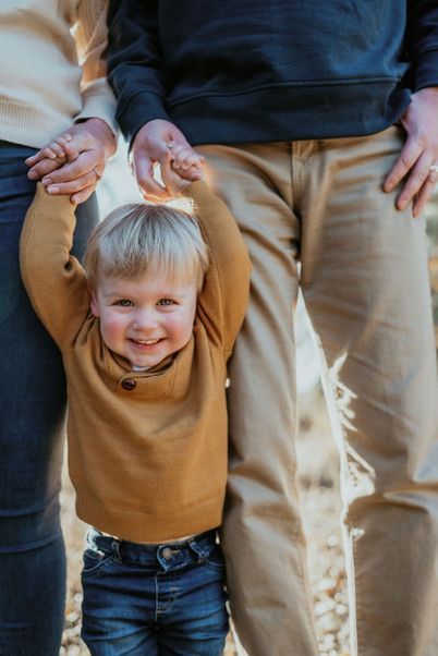 a little boy holding the hands of his parents