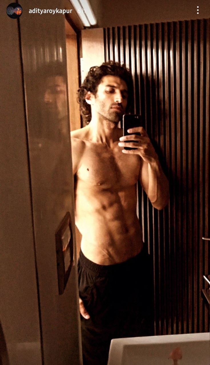 a shirtless man taking a selfie in front of a mirror with his cell phone