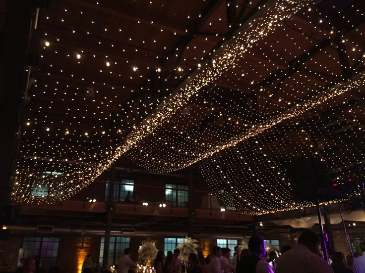 the ceiling is covered with lights and people are standing in front of it at night