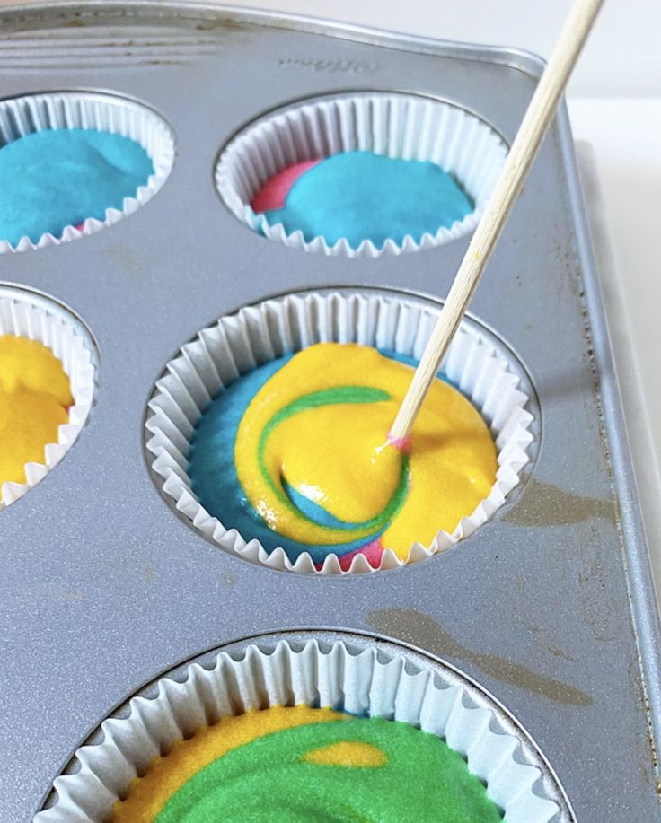 cupcake tins with blue and green frosting in them being filled with batter