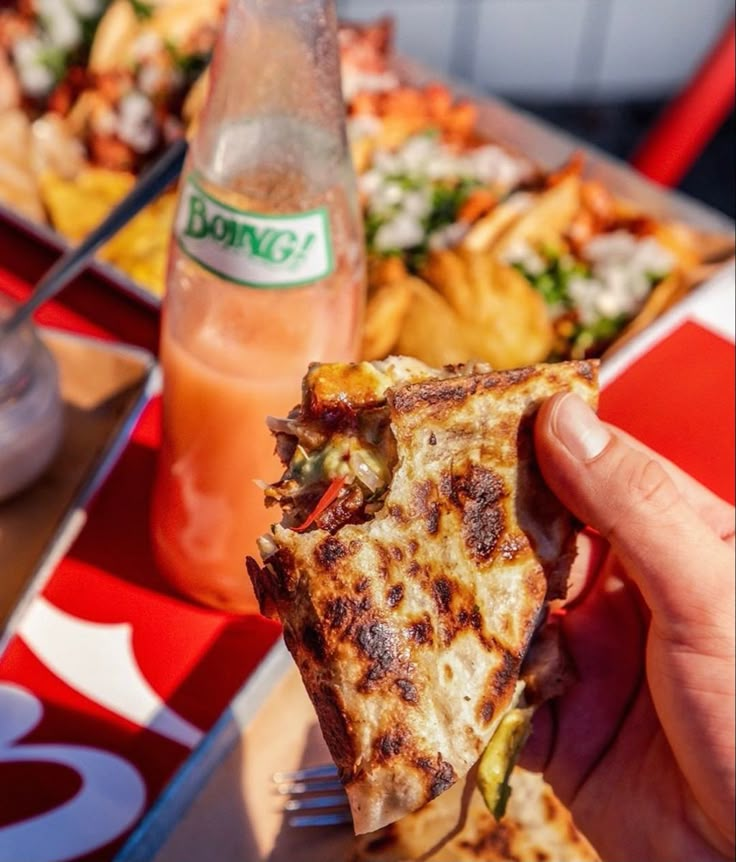 a person holding a slice of pizza in front of a table full of food and drinks