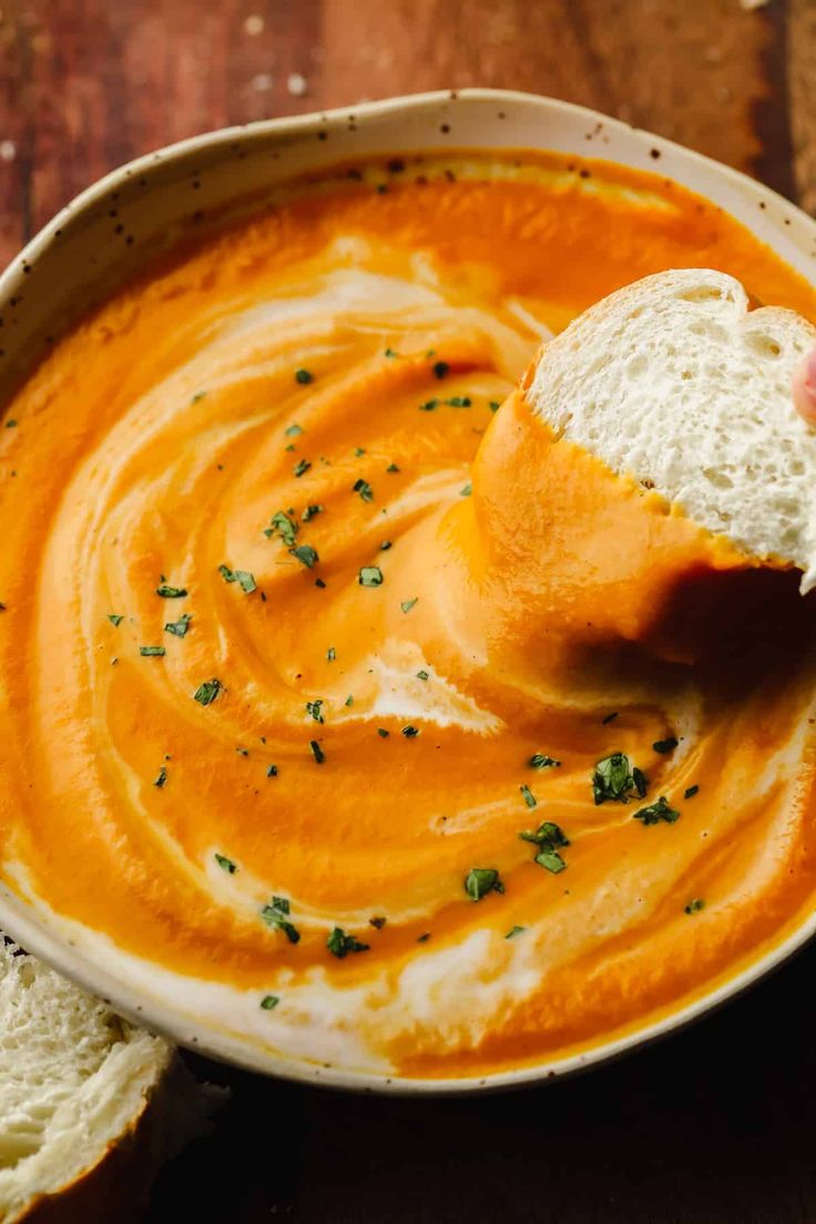 a bowl of soup with bread in it and a piece of bread on the side