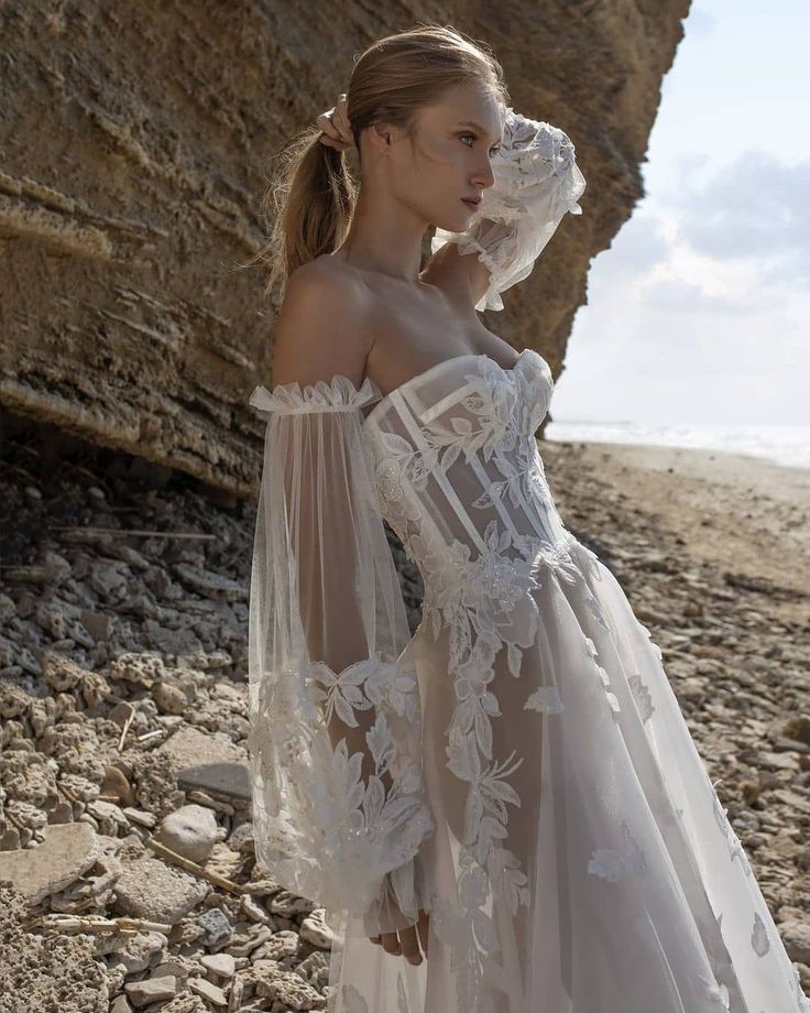 a woman standing on top of a rocky beach next to the ocean wearing a white dress