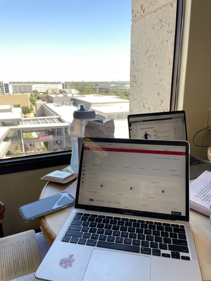 an open laptop computer sitting on top of a desk next to a book and cup