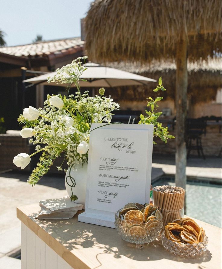 a table with some food on it next to a sign and flowers in a vase