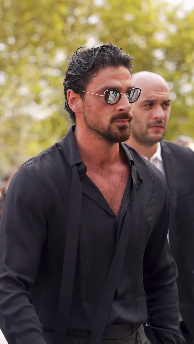 a man with sunglasses on his face walking in front of another man wearing a suit and tie