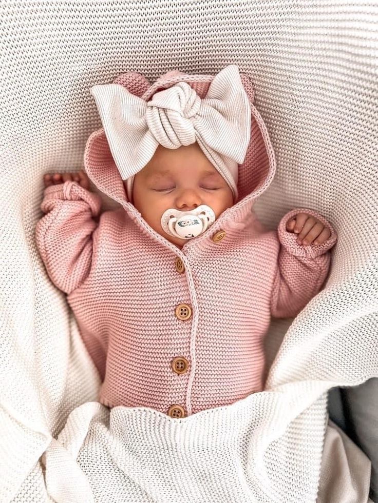 a baby is wearing a pink sweater and a white bow