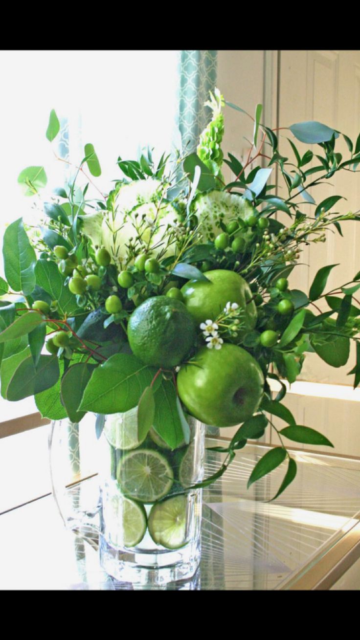 a glass vase filled with green fruit and greenery