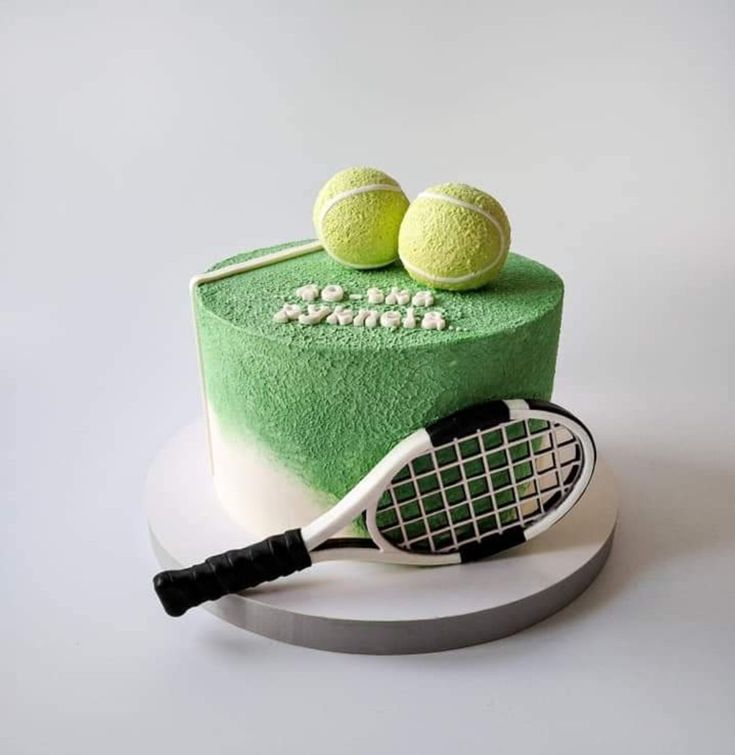 a green cake with tennis balls and racquets on top, sitting on a plate