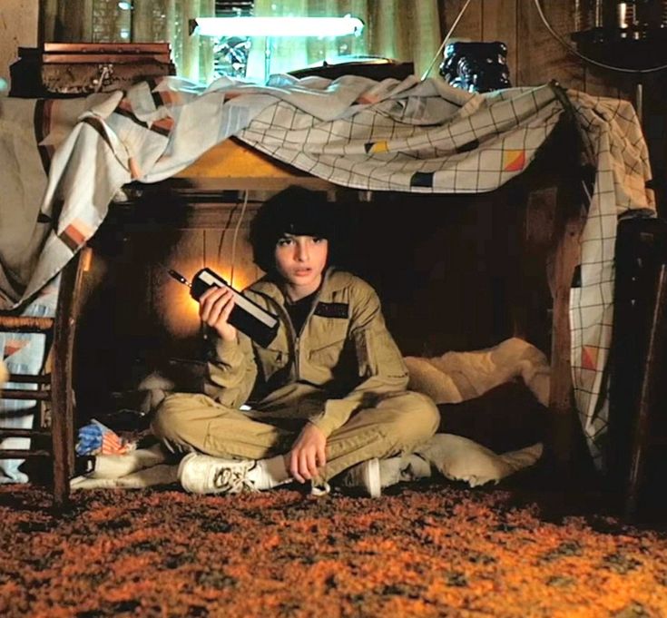 a young man sitting on the floor in front of a bed holding a remote control