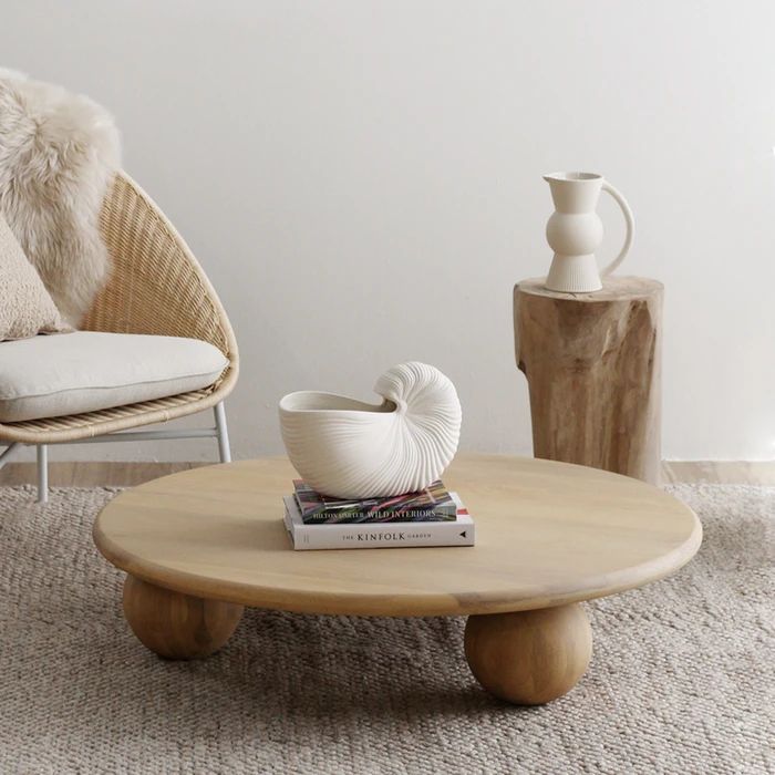 a white vase sitting on top of a wooden table next to a chair and ottoman