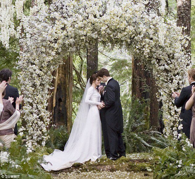 a bride and groom standing in front of an archway with white flowers on the side