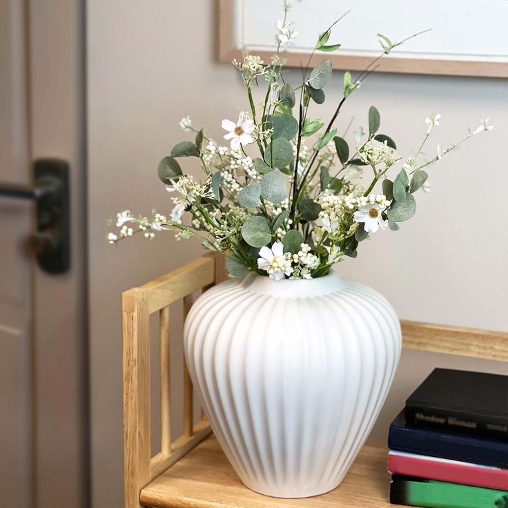 a white vase filled with flowers sitting on top of a wooden table next to books