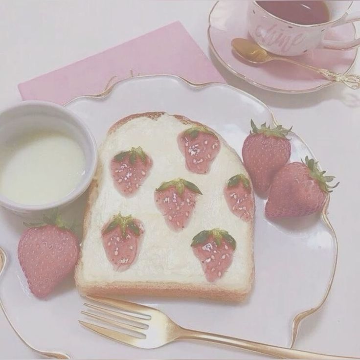 a piece of bread with strawberries on it next to a cup of milk and two forks