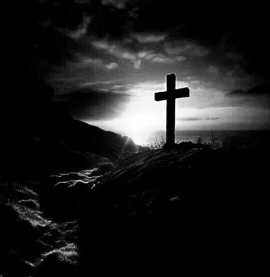 a black and white photo of a cross on top of a hill with the sun behind it