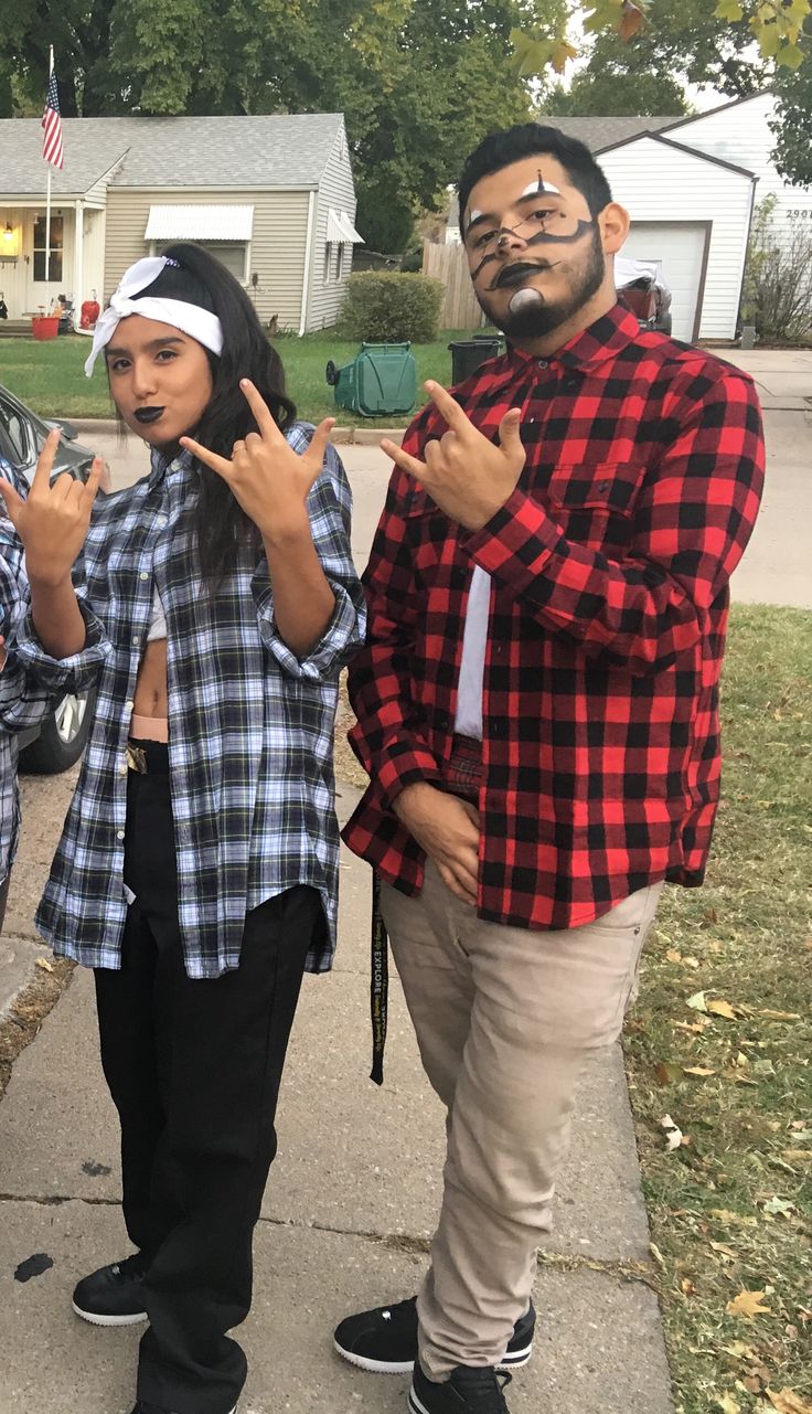 two people standing next to each other in front of a house making the peace sign