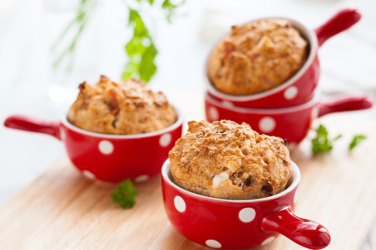 three red mugs filled with muffins on top of a wooden cutting board