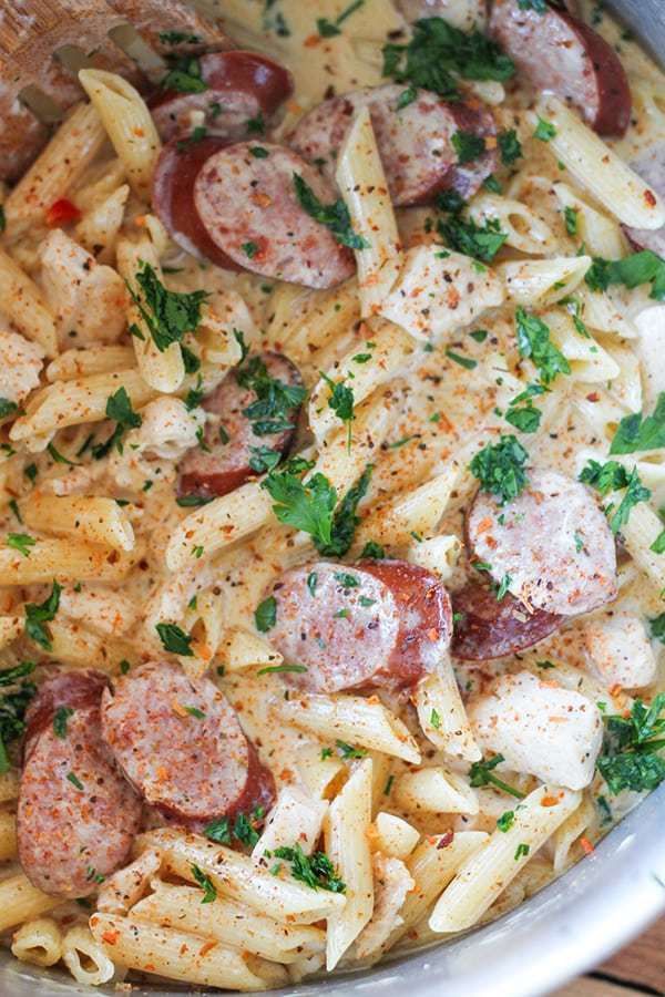 pasta with sausage and parsley in a pan on a wooden table, ready to be eaten