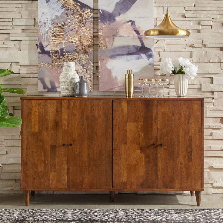 a wooden cabinet sitting in front of a brick wall with paintings on the wall behind it