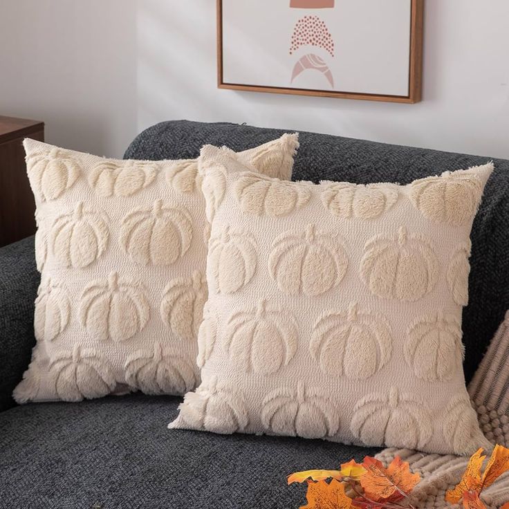 two pillows sitting on top of a couch next to a vase with flowers in it