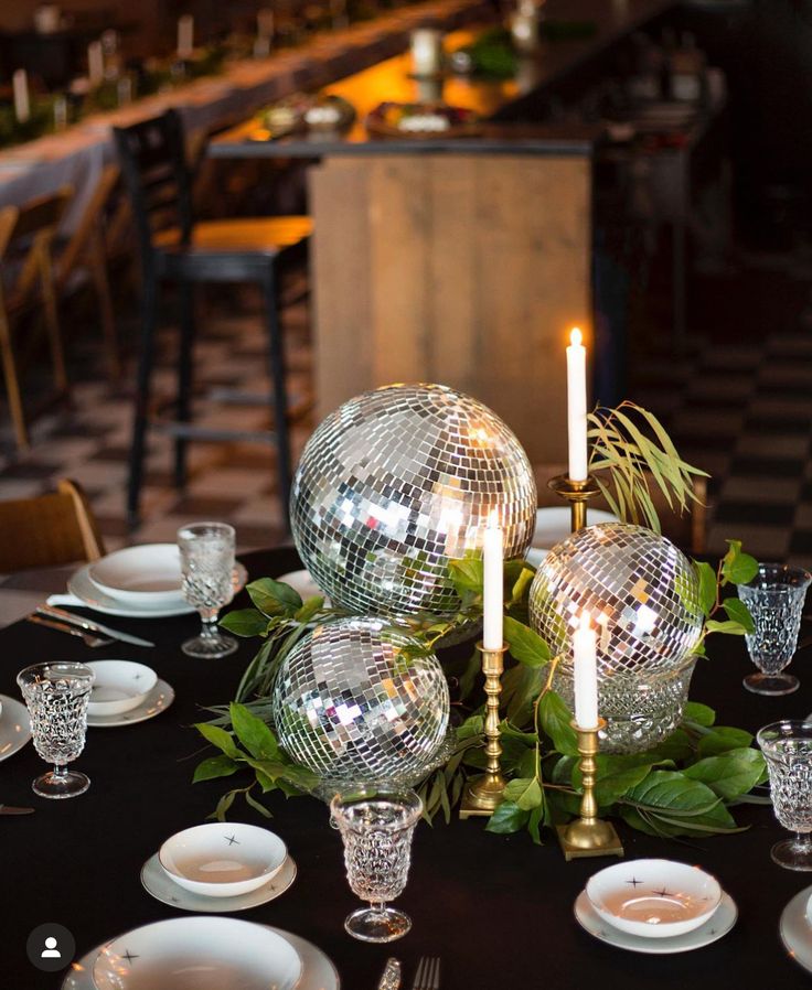 a table topped with plates and glasses filled with disco ball decorations on top of a black table cloth