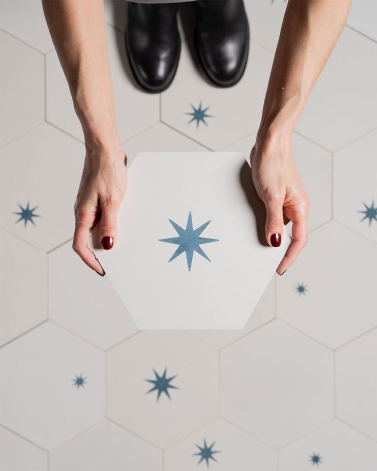 two hands holding a piece of paper with blue stars on it in front of a tiled floor