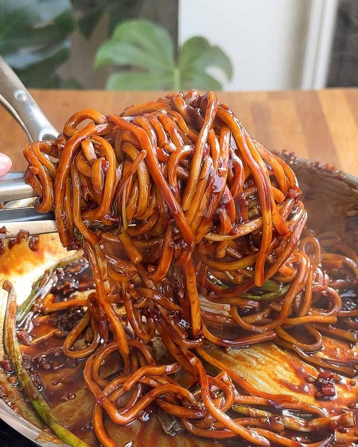 someone is holding tongs over some noodles in a pan on the table with other food items