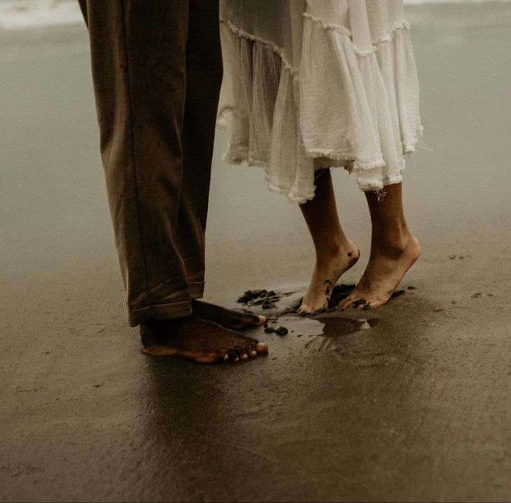 two people standing next to each other on the beach with their feet in the sand