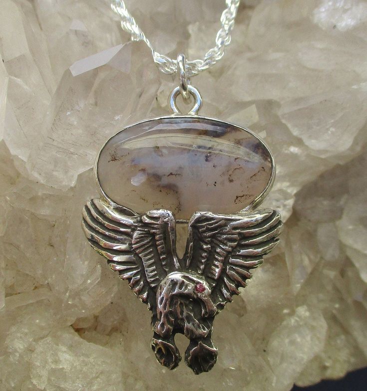 This is a unique Sterling Silver spread wing Eagle necklace that is set with a Dendritic Agate from Oregon and it has a Ruby set in the eye of the Eagle. My husband cut and polished the Oregon Agate and we collaborated on the design. The Agate is oval shape that measures 25mm by 14mm. It is bezel set with an open back. The Eagle is hand cast and antiqued to bring out the high lights in the design. A small round natural Ruby is set in the eye. It is about 1mm round. The Eagle has a soldered loop Eagle Pendant, Ruby Set, Eagle Necklace, Handmade Hoop Earrings, White Beaded Necklaces, Sterling Silver Wire Wrap, Dendritic Agate, The Eagle, Tourmaline Crystal