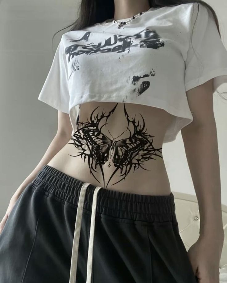 a woman wearing a white crop top and black shorts with an antelope tattoo on her stomach