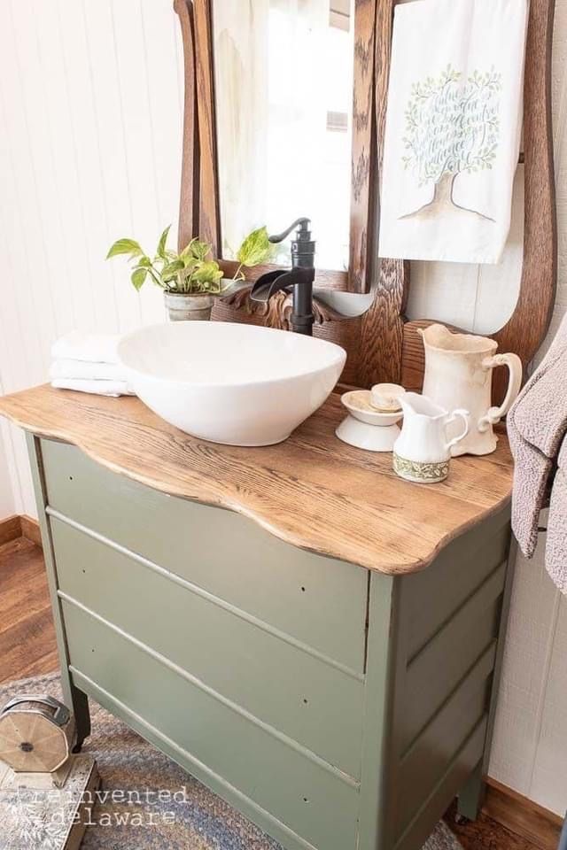 a bathroom sink sitting on top of a wooden counter next to a mirror and potted plants