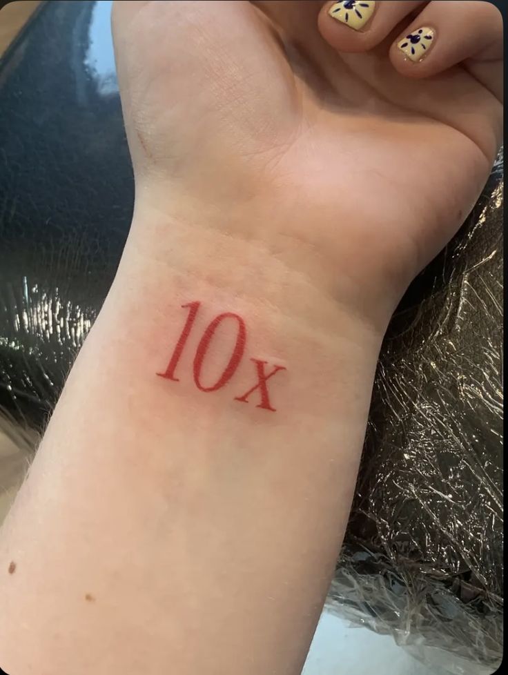 a woman's wrist tattoo with the number 10 on her left arm and red ink that reads 10x