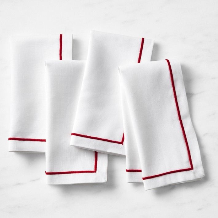 four white napkins with red stitching are on a marble countertop and one is folded in half