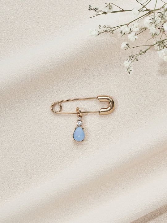 a blue stone is attached to a gold colored metal pin with a white flower in the background