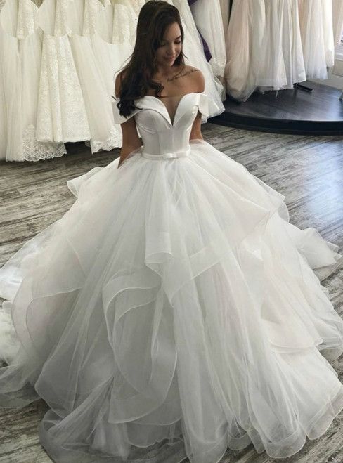 a woman in a white wedding dress is looking at the dresses on display behind her