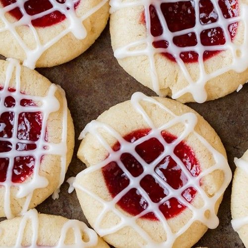 several cookies with white icing and red jelly in the middle on a baking sheet