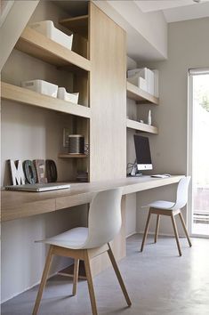 a desk with two chairs and a laptop on it in front of a wall mounted bookcase