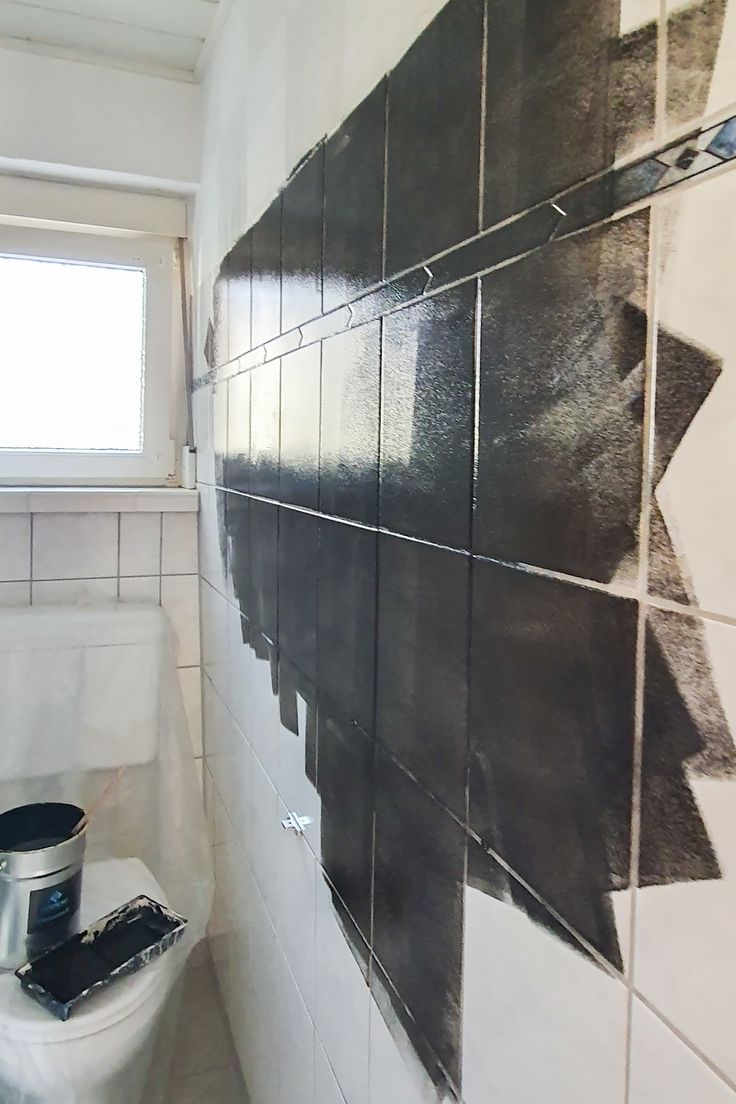 a white toilet sitting next to a black and white tiled wall in a bathroom under a window