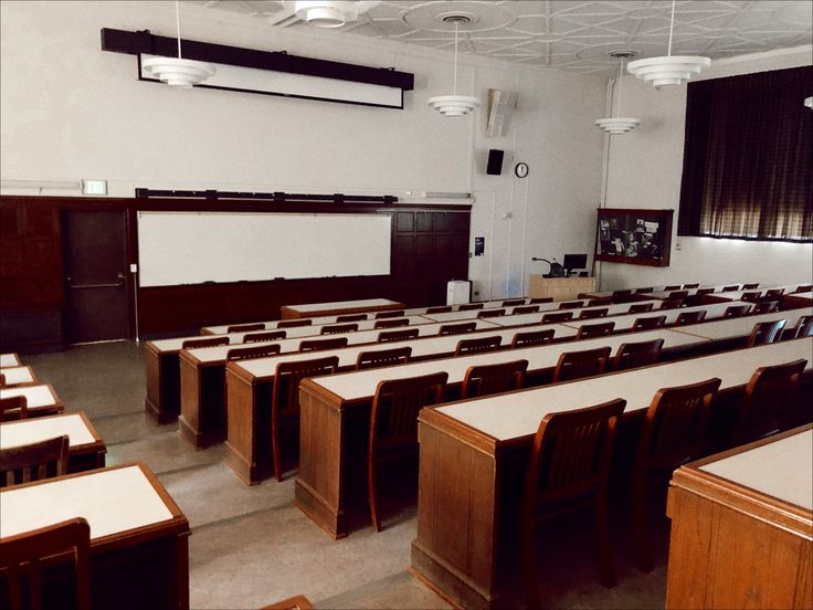 an empty classroom with wooden desks and whiteboards on the wall, in front of a projector screen