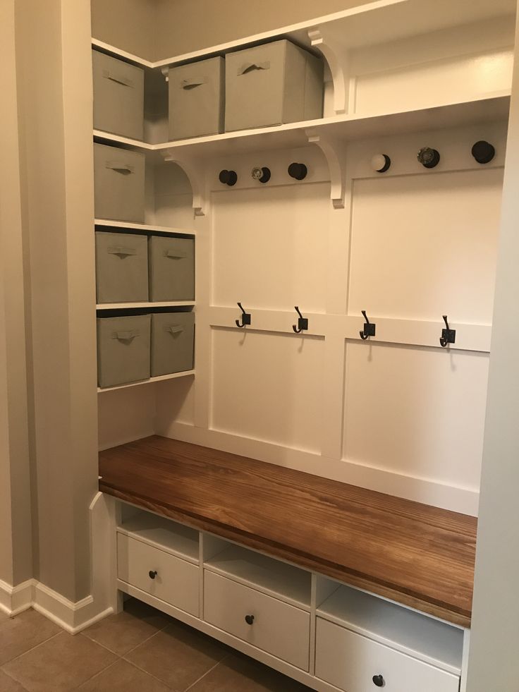 an empty room with white cabinets and wooden bench in the center, filled with storage bins