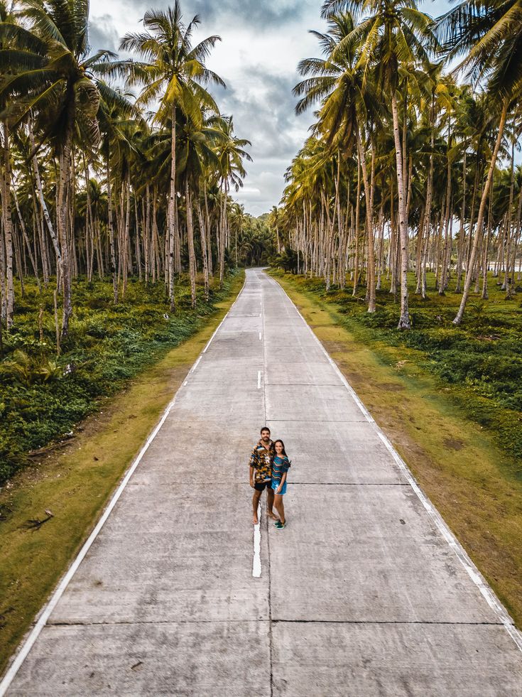 a person standing in the middle of an empty road with palm trees on both sides