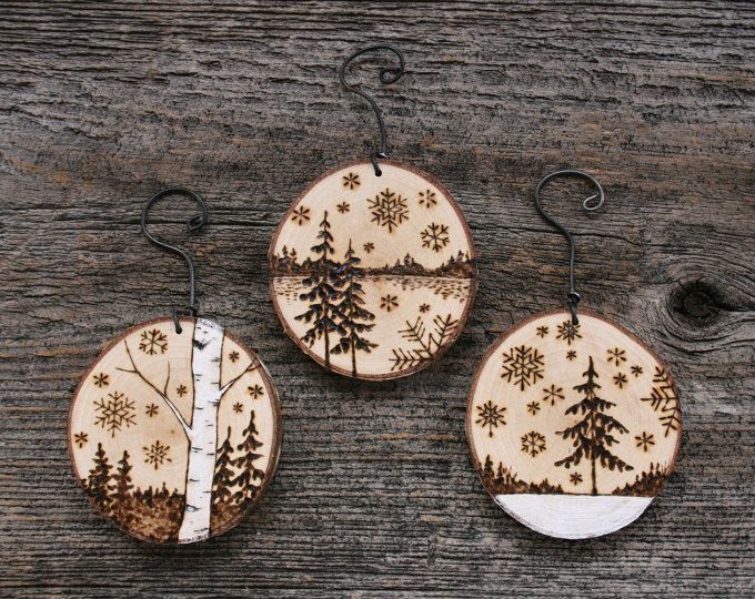 three wooden ornaments with trees and snowflakes hanging from hooks on a wood surface