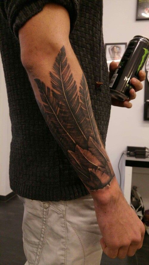 a man with a feather tattoo on his arm holding a can and a cell phone