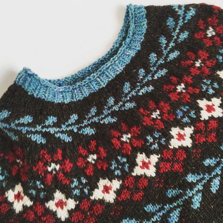 a close up of a sweater on a white surface with blue, red and black designs