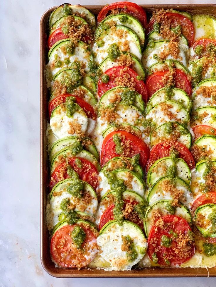 a pan filled with sliced cucumber and tomato slices covered in cheese, seasoning and herbs