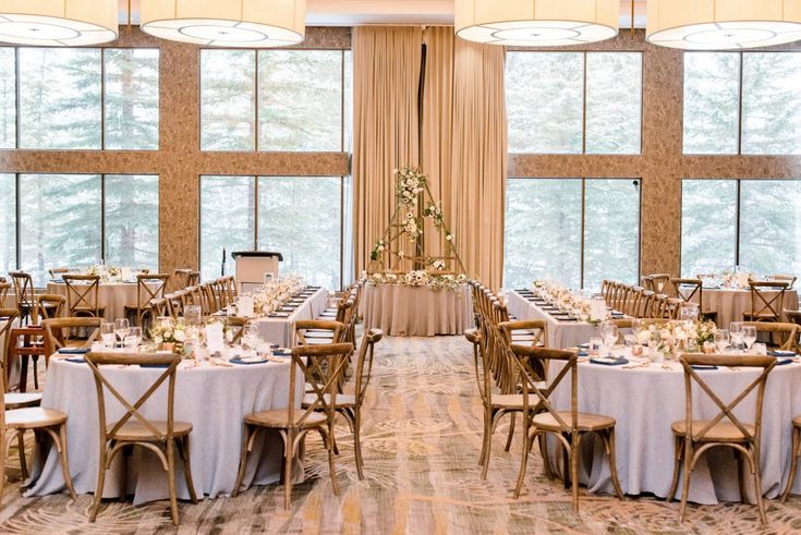 a room filled with lots of tables covered in white tablecloths and wooden chairs